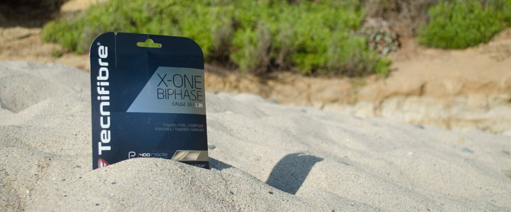 A photograph of the the front of Tecnifibre X-One Biphase in the sand at the beach on a sunny day.